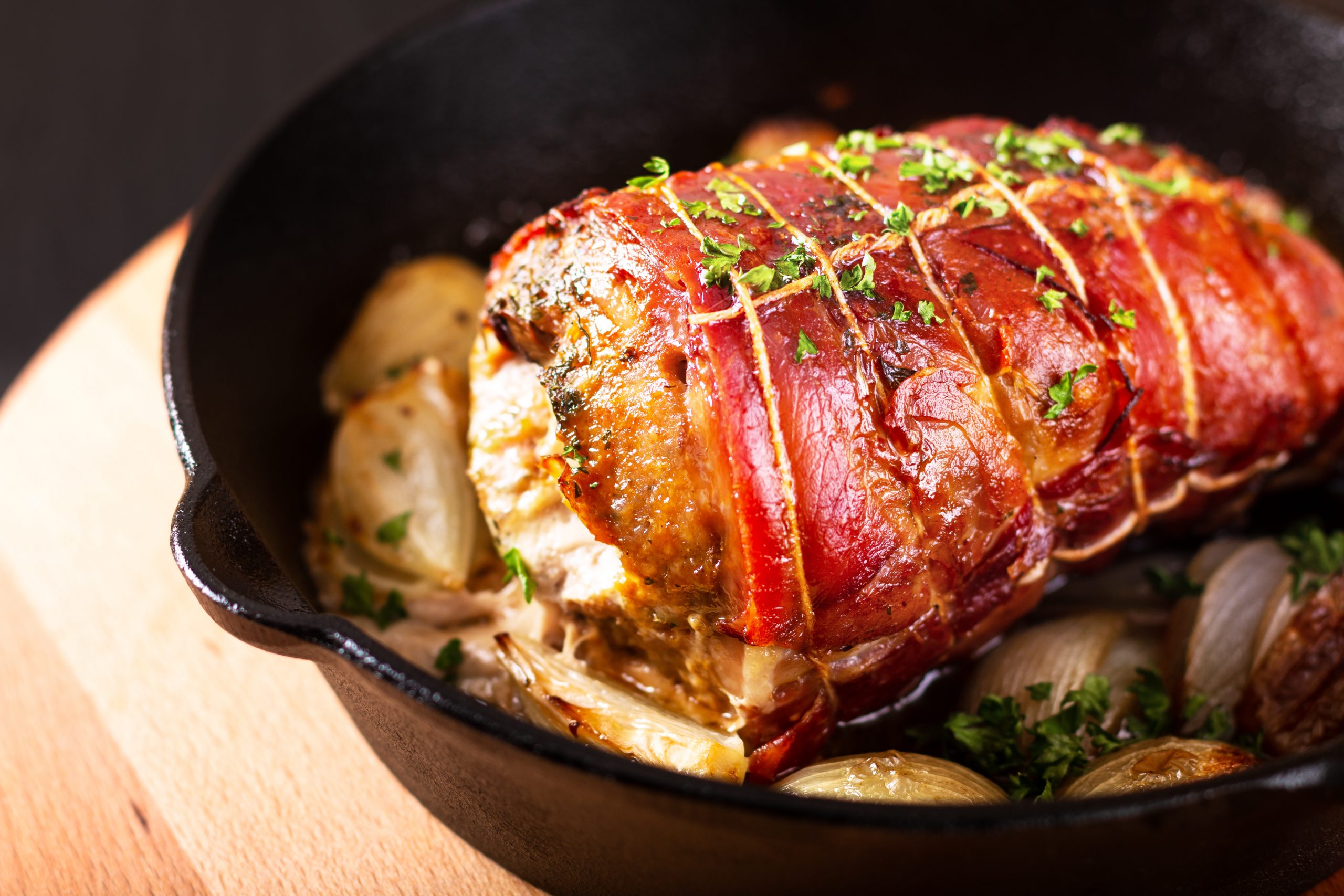 Food concept homemade Bacon Stuffed Pork Tenderloin baked in iron cast skillet on round wooden board